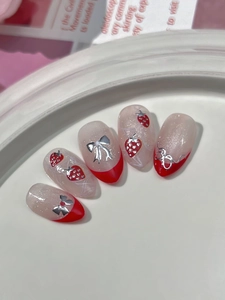 Detail of red French tip press-on nails with strawberry art and silver 3D bows