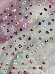 Macro detail of strawberry and bow nail art stickers with metallic texture and 3D glaze