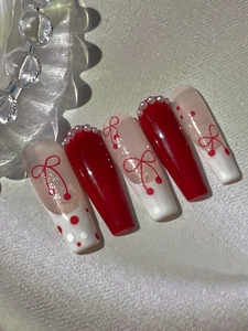 Detail of red and white bow nail art with pearl accents on long coffin shaped nails
