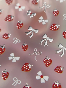 Macro shot of 3D strawberry and metallic silver bow nail art charms on pink background
