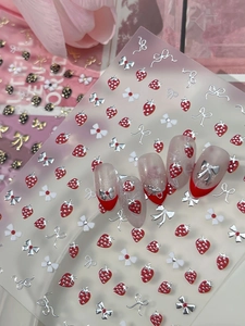 Macro detail of 3D nail art stickers featuring red strawberries and white bow designs