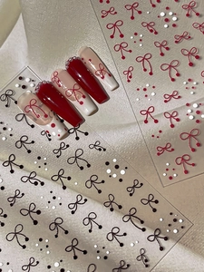 Detail of 3D bow and dot nail stickers with珍珠 accents on red and nude manicure