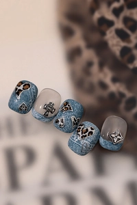 Macro view of denim texture nail tips featuring leopard hearts and metal cross charms