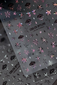 Macro detail of holographic nail art stickers featuring stars, clouds and text elements