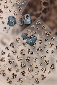Detail of leopard print heart nail stickers with gold edges and metallic cross charms