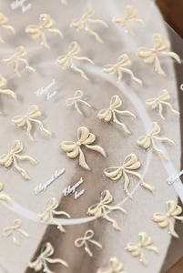 Macro shot of 3D embossed pearlescent bow nail stickers with elegant cream finish