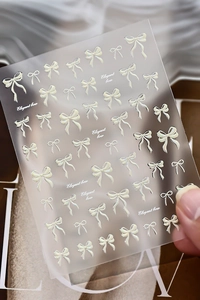 Close-up of 3D cream bow nail stickers with pearl finish on soft fabric background