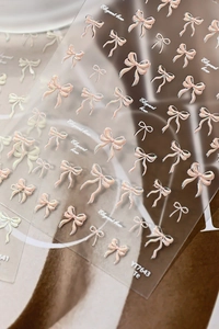 Macro view of 3D embossed nail art stickers featuring pink and pearl white bows