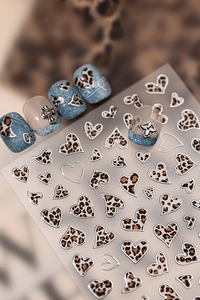 Detail of leopard print heart nail stickers with silver metallic borders on denim blue nails