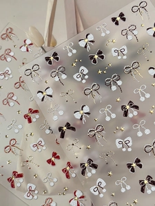 Detail of 3D gold embossed bow and star nail art stickers in cream and burgundy red