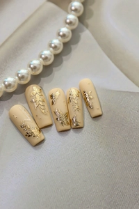 Macro view of matte beige press-on nails with golden floral and butterfly relief details
