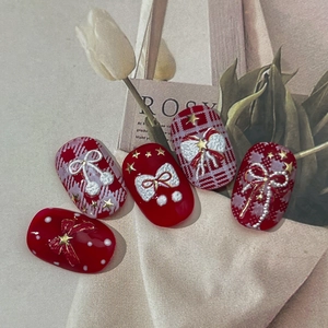 Festive red and white press-on nails with 3D bows, metallic stars, and classic plaid patterns
