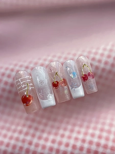Close-up of pink glitter press-on nails with 3D cherry accents and white snowflakes