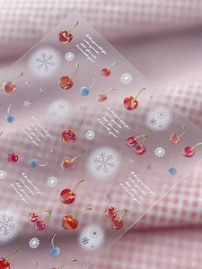 Detail of red cherry and white snowflake nail stickers with a glossy finish