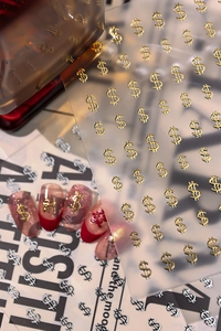 Macro view of golden dollar sign and Chinese character nail stickers on red manicure