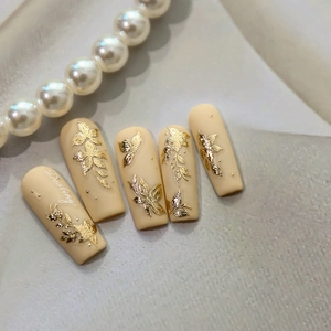 Press-on nails featuring 3D gold embossed flowers and butterflies on matte nude base