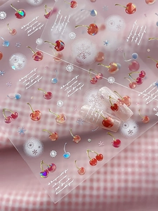 Macro shot of 3D cherry and snowflake nail art stickers with elegant cursive text