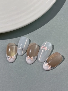 Detailed view of cat-eye nails with 3D pink bows and silver heart charms on grey surface