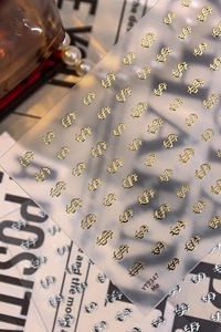 Macro shot of gold dollar sign nail stickers with 3D embossed metallic texture on sheets
