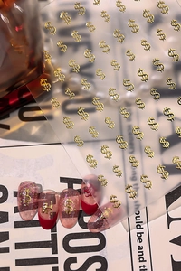Close-up of golden dollar sign nail art stickers with French red and nude glitter finish