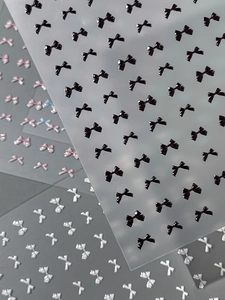 Detailed macro view of 3D embossed bow nail stickers in black, pink, and white colors