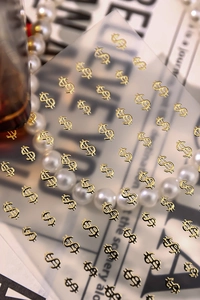 Macro shot of gold dollar sign nail stickers with shiny 3D relief texture for DIY nail art