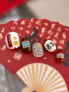 Macro shot of 5 New Year nail charms with lucky text and gold coin patterns on red fans