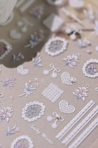Detail of 3D embossed nail stickers with white lace, floral motifs and pearl bow designs