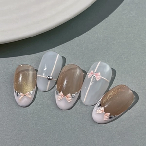 Nude pink cat-eye press-on nails with 3D pink bows and silver bead embellishments