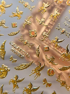 Macro shot of gold 3D embossed nail stickers featuring celestial horse and wing motifs