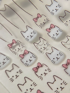 Close-up of 3D embossed white cat nail art stickers with cute pink bows and fuzzy texture