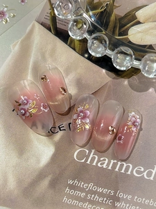 Macro detail of almond nails with 3D white flowers, pearls and gold foil on pink gradient
