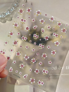 Detail showing pink floral nail decals with golden outlines and delicate gradient petals
