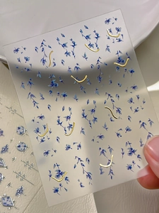 Detail of blue floral nail stickers with gold foil lines held over white background