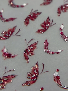 Macro shot of 3D butterfly nail art stickers in deep red with silver metallic glitter details