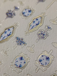 Macro detail of 3D embossed nail stickers with blue flower motifs and gold foil edges