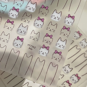 Cute white cartoon cat face nail art stickers with purple bows on a matte sheet