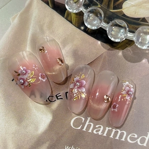 Pink gradient press-on nails with 3D floral accents and gold leaf on silk background