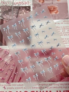 Makroaufnahme von 3D-Nagelstickern mit blau-weißen Schleifen und kleinen Glitzersteinen