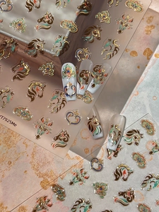 Detail of gold foil horse nail stickers with vintage patterns on white nail tips