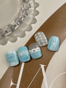 Dettaglio di unghie finte blu e grigie con fiocchi in resina 3D e motivi in pizzo