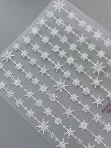 Close-up of 5D white snowflake nail stickers with embossed relief texture on grey background