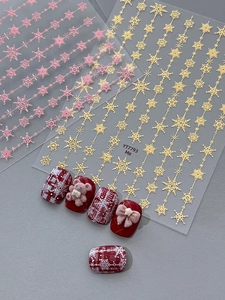 Macro view of snowflake nail decals with gold and pink embossed patterns on burgundy nails