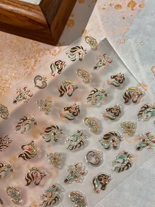Detailed close-up of metallic horse and heart nail stickers with champagne gold outlines