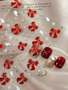 Macro shot of 3D Christmas nail stickers with red bows and white snowflakes on nails