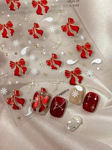Macro detail of 3D red bow and white snowflake nail stickers with gold star patterns