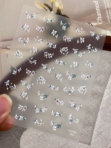 Detailed macro shot of white floral nail stickers with green leaves on model's hand