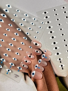Close-up of blue Evil Eye nail stickers on transparent backing and natural manicure