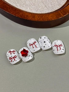 Detail of white nail patches with black polka dots, red bows, and a 3D star gem