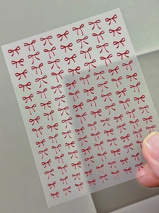 Macro shot of 3D embossed red bow nail art stickers on translucent matte backing